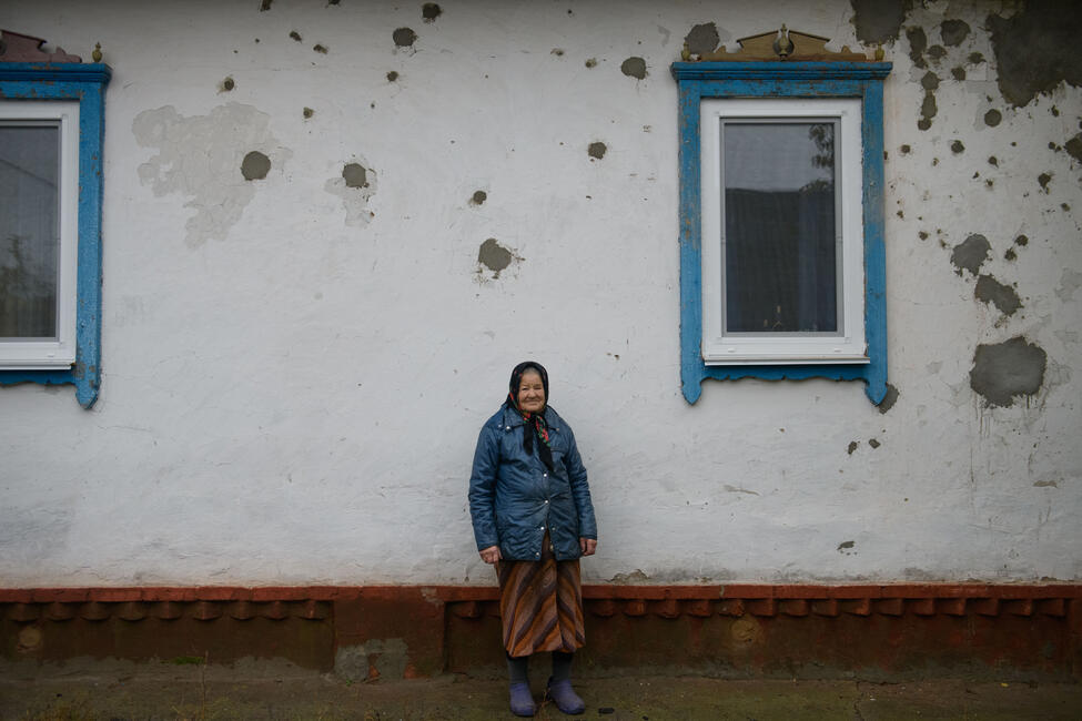 Eine ältere Frau vor einem Haus mit Einschusslöchern