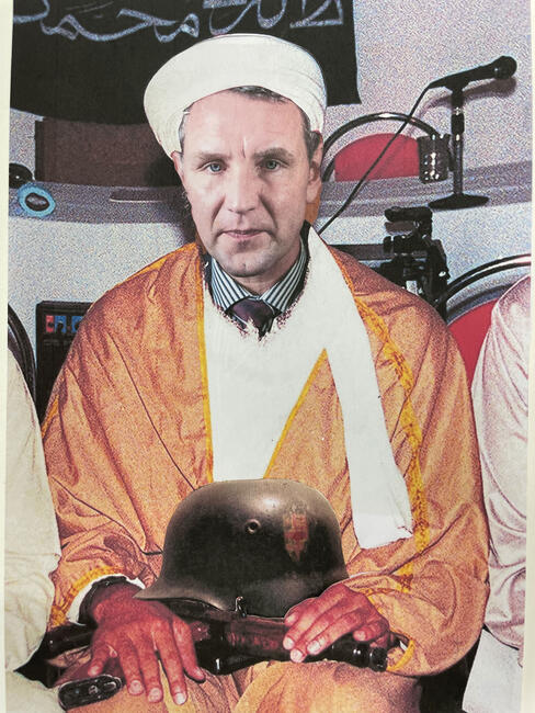 Das Bild zeigt einen Mann, der einen Turban trägt. Ein Soldatenhelm liegt auf seine Schoß