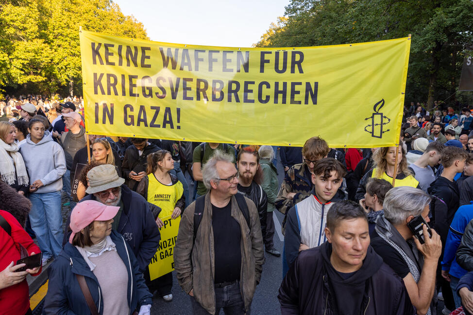 Das Foto zeigt mehrere Personen in einer riesigen Menschenmenge, die ein Banner hochhalten mit Amnesty-Logo und dem Schriftzug "Keine Waffen für Kriegsverbrechen in Gaza!"