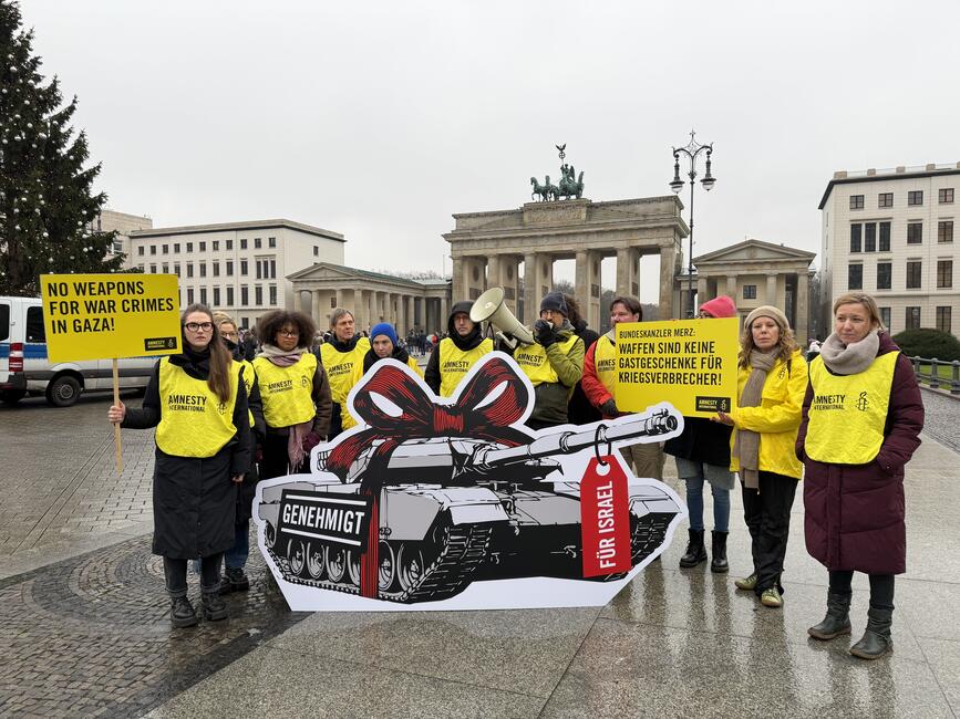 Mehrere Menschen mit gelben Leibchen mit der Aufschrift "Amnesty" und Protestplakaten