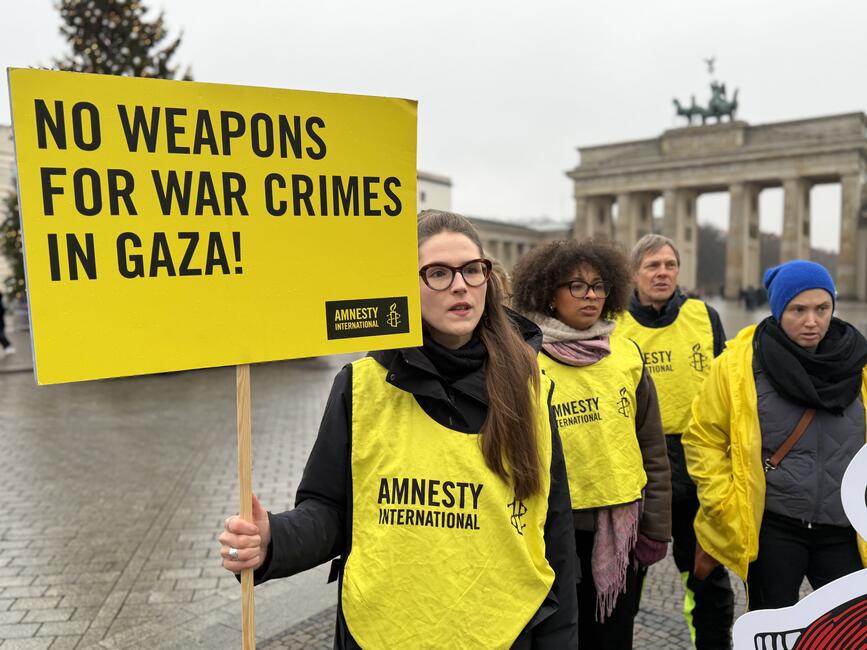 Mehrere Menschen mit gelben Leibchen mit der Aufschrift "Amnesty" und Protestplakaten