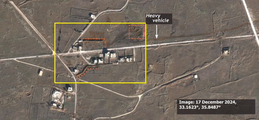 Satellitenbild desselben Gebiets in Al-Hamidiya vom 17. Dezember 2024. Orange gestrichelte Linien und Markierungen heben neue Fahrspuren schwerer Fahrzeuge sowie neu aufgeschüttete Erdwälle rund um die noch stehenden Gebäude hervor.