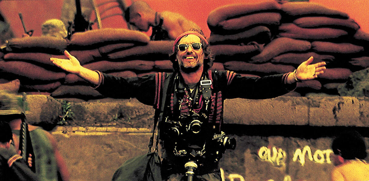 Dennis Hopper breitet in einer Szene aus Apocalypse Now seine Arme aus und lacht.