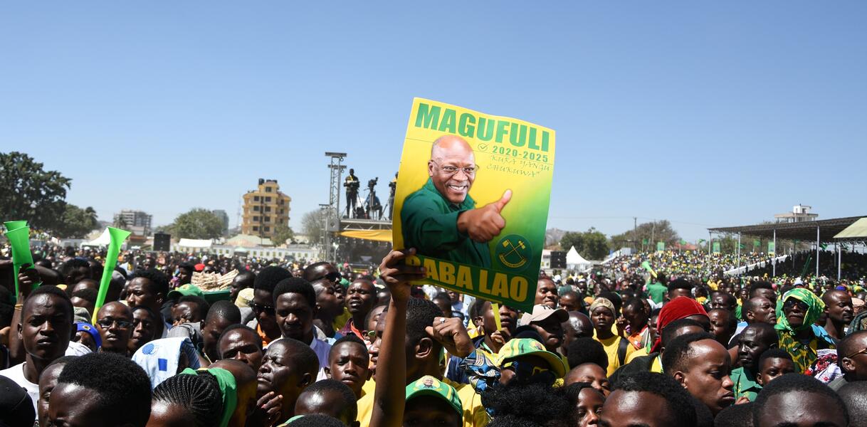 Das Foto zeigt eine Menschenmenge. Im Vordergrund hält ein Mann ein Plakat mit der Aufschrift Magafuli für den Präsidentschaftskandidaten der Regierungspartei in die Höhe.