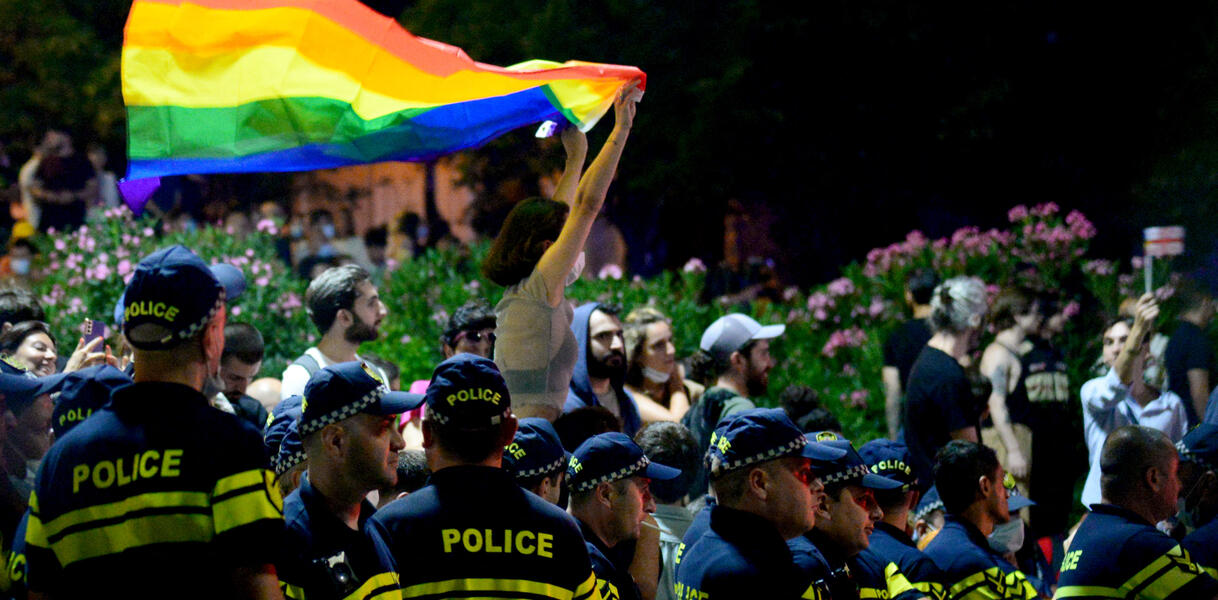 Eine Frau hält eine Regenbogenfahne über den Kopf. Sie ist von uniformierten Polizisten umgeben.