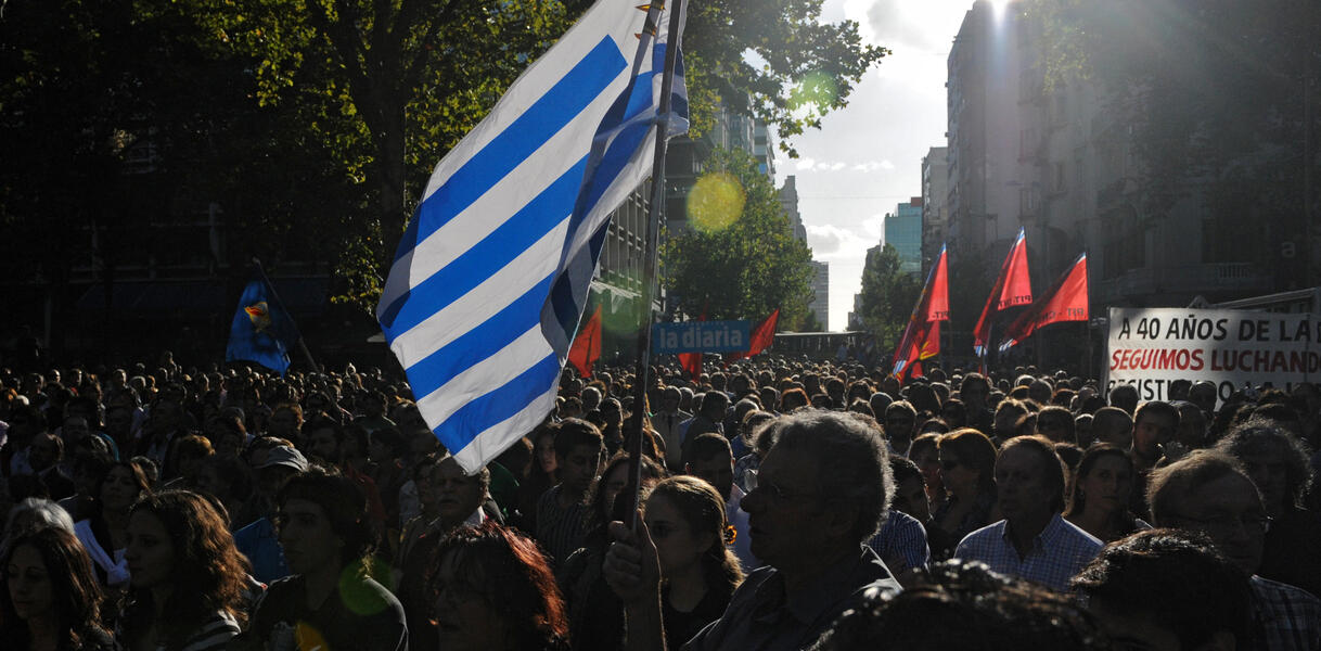 Eine Menschenmenge auf einer Straße, in der Mitte eine Fahne Uruguays. 