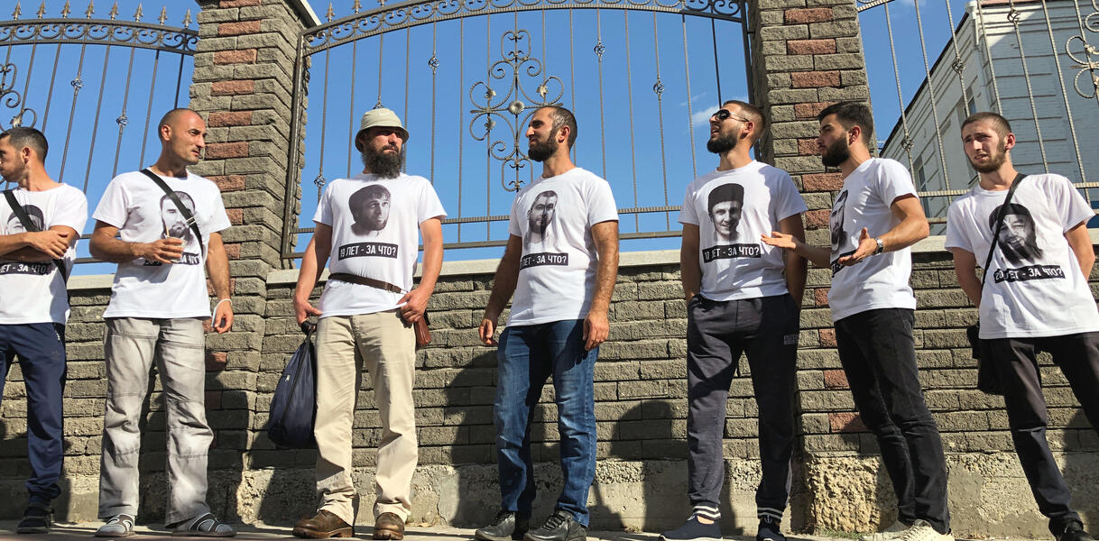 Männer in T-Shirts stehen vor einem Zaun vor einem Gerichtsgebäude.