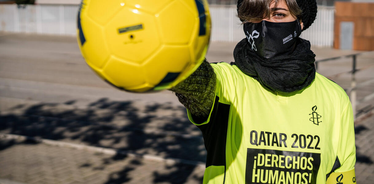 Das Bild zeigt eine junge Frau mit einem Fußball in der Hand und einem gelben Amnesty-T-Shirt an, darauf steht "Katar 2022. Menschenrechte!"