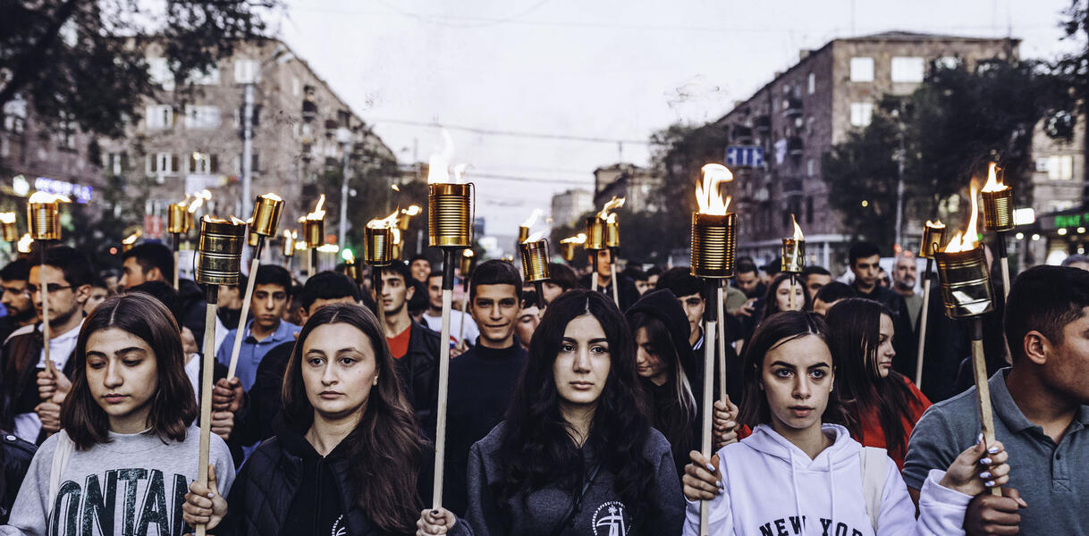 Das Bild zeigt frontal eine Menschenmenge mit Kerzen und Fackeln auf einer Straße