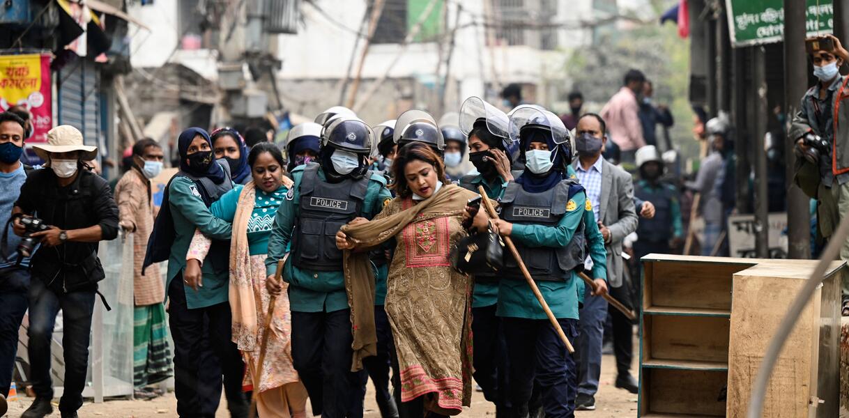 Auf einer staubigen Straße werden Frauen von uniformierten Polizisten abgeführt.