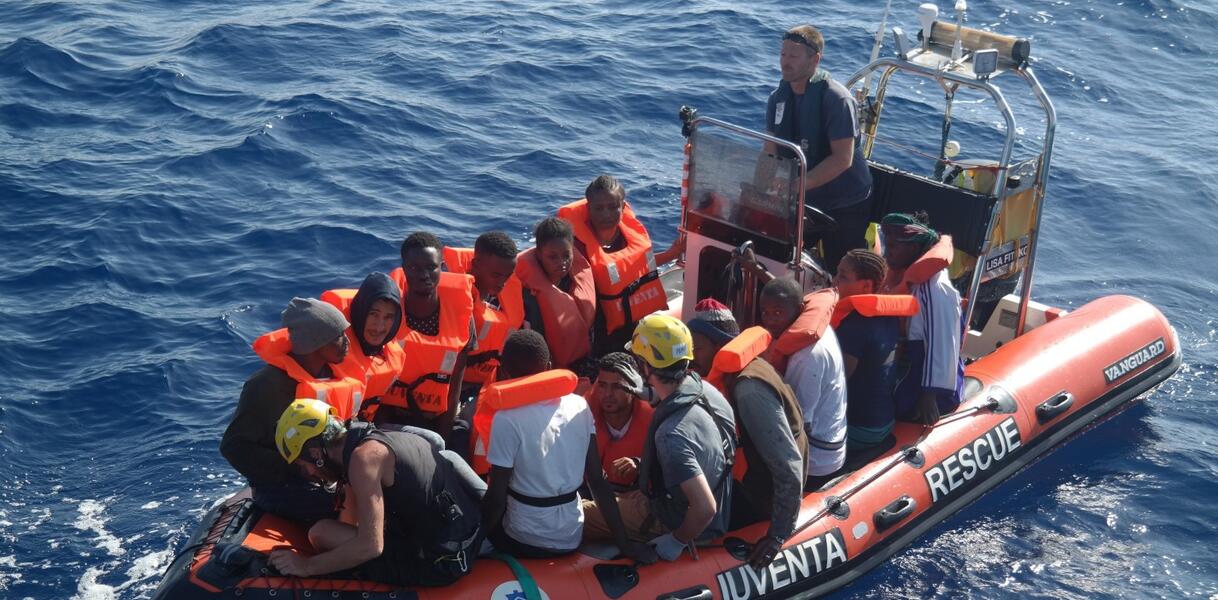 Das Bild zeigt ein Rettungsboot im Meer, mit vielen Menschen, die Rettungswesten tragen 