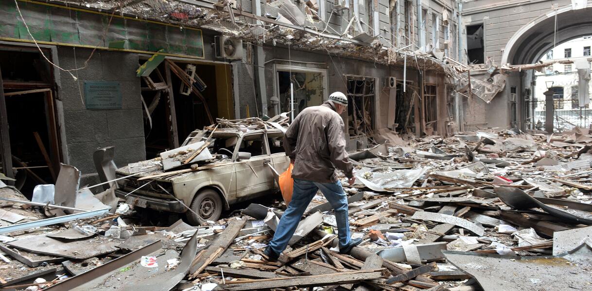Das Bild zeigt eine Person, vor einem vollständig zerstörten Gebäude