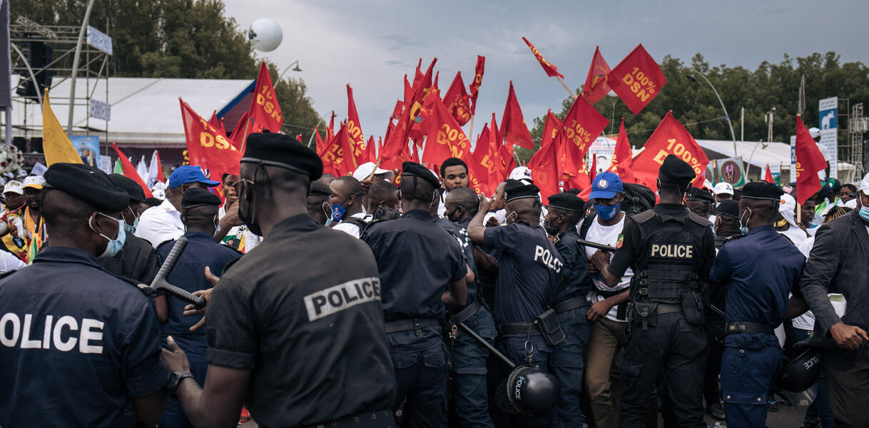 Eine Menschenmenge aus Polizisten und Zivilist_innen mit roten Fahnen