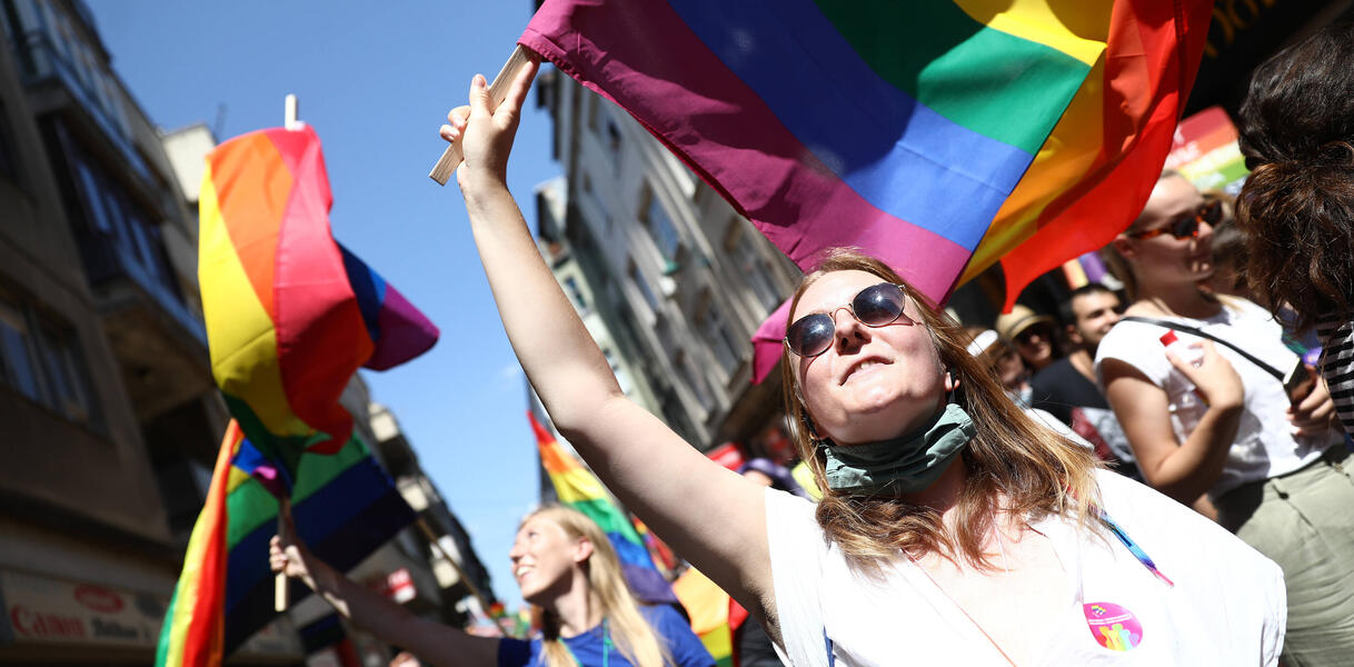 Zentral im Bild schwenkt eine junge Frau eine Regenbogenfahne. Im Hintergrund befinden sich weitere Demonstrant_innen.