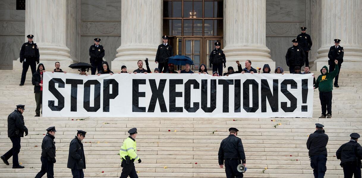 Das Bild zeigt mehrere Menschen, die ein großes Banner mit der Aufschrift "Stop Executions" in der Hand halten