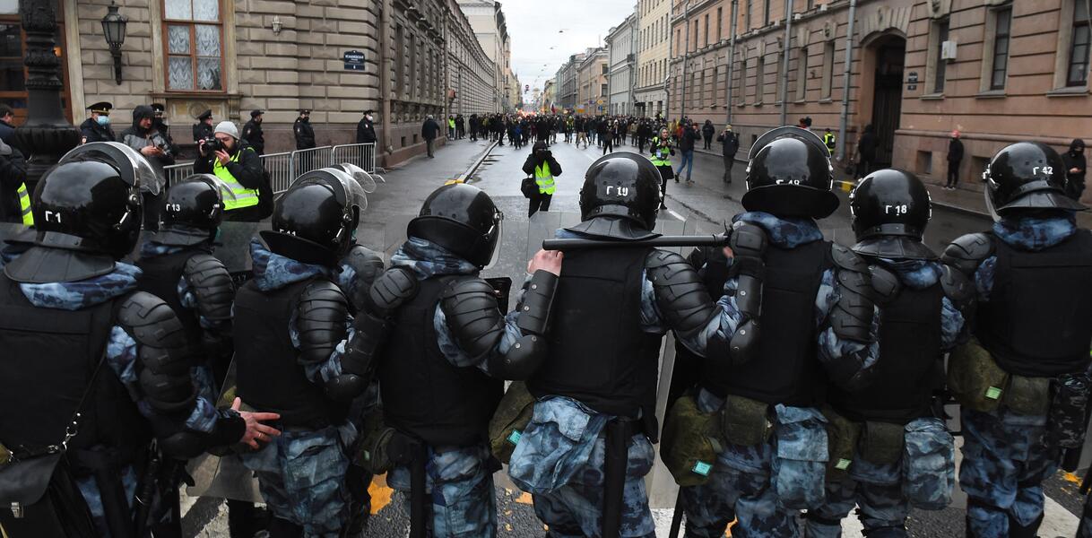 Das Bild zeigt schwer ausgerüstete Polizisten im Vordergrund, eine Menschenmenge im Hintergrund