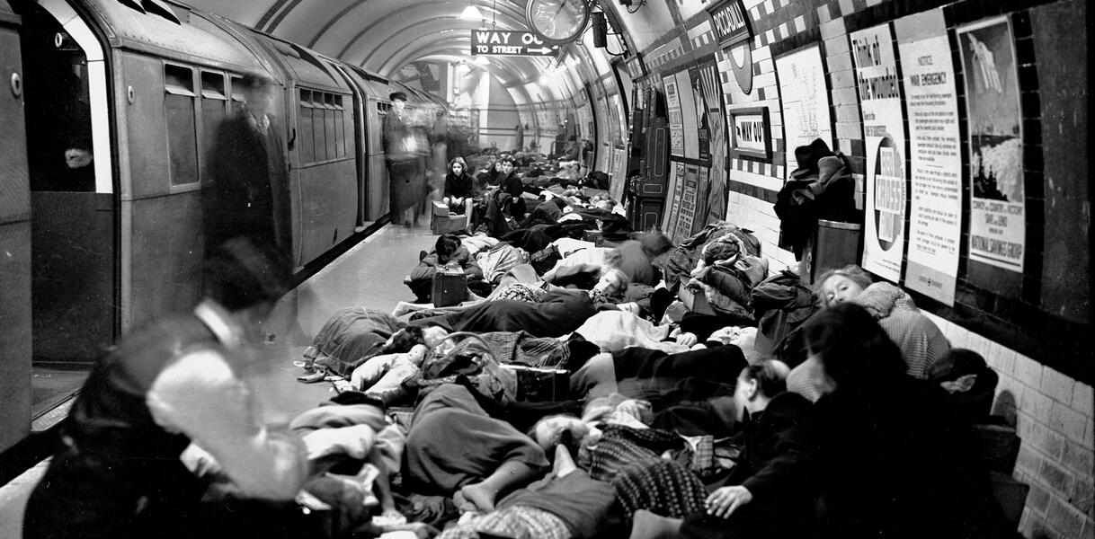 In einer Londoner U-Bahn-Station steht eine U-Bahn am Gleis, Menschen liegen auf dem Bahnsteig dicht an dicht.