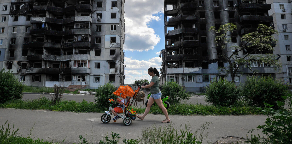 Eine Frau mit Kinderwagen vor zerstörten Hochhäusern