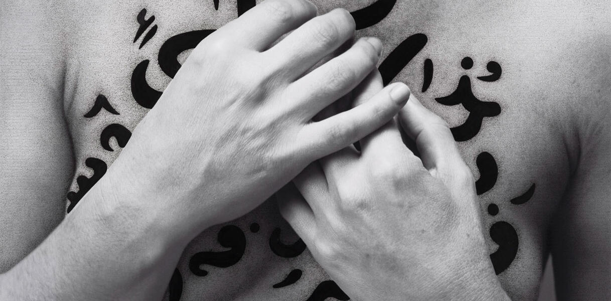 Arabische Schriftzeichen auf der Brust einer Frau, die ihre Hände davor verschränkt hält.