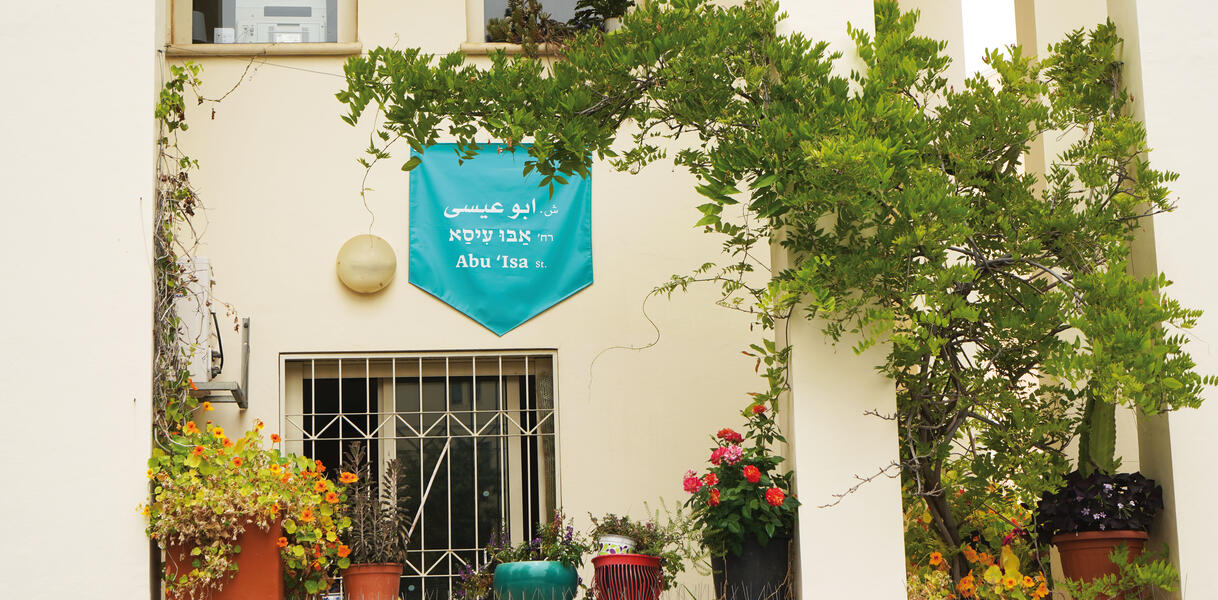 Eine Straße in Israel, an einem Haus hängt ein Banner, auf dem der Straßenname auch auf Arabisch zu lesen ist, Abu Isa.