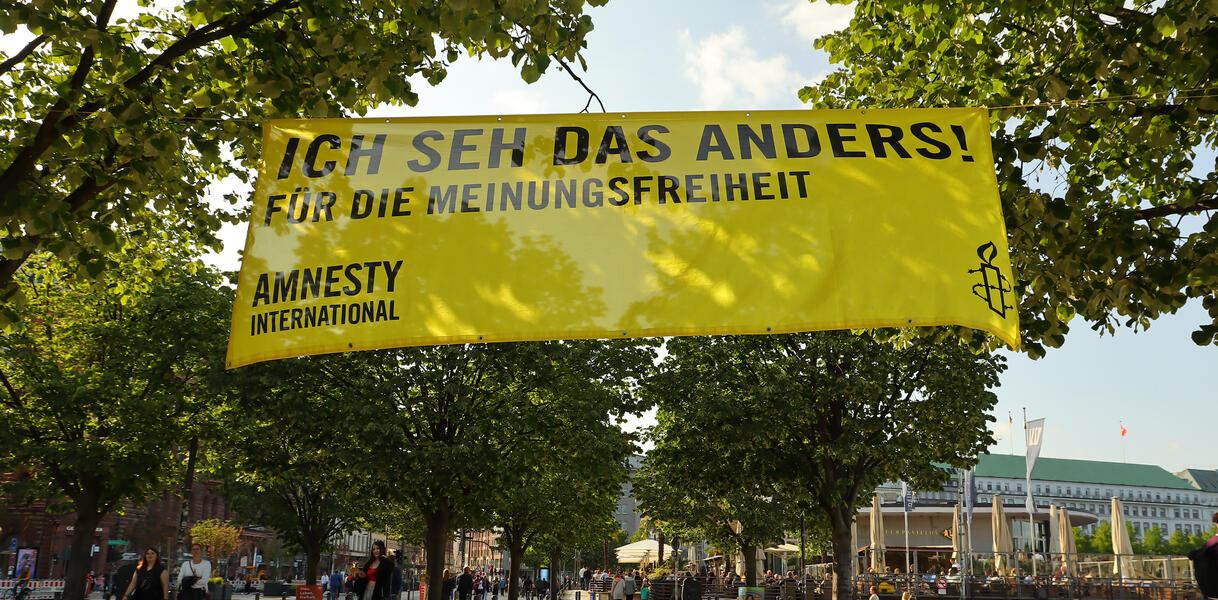 Das Bild zeigt ein Banner mit der Aufschrift "Ich seh das anders", das an Bäumen befestigt ist.