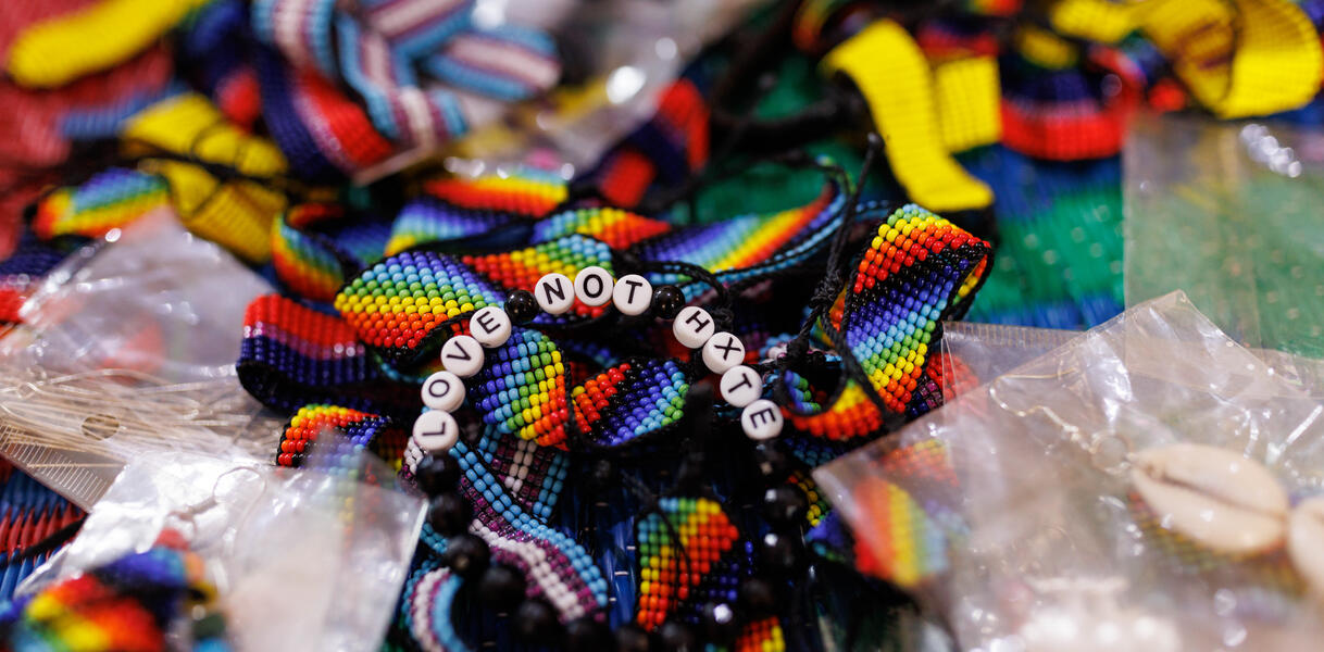 Das Bild zeigt eine Armband in Regenbogenfarben. In das Band sind kleine Steine mit Buchstaben eingewoben. Sie bilden den Satz: "Love not hate".
