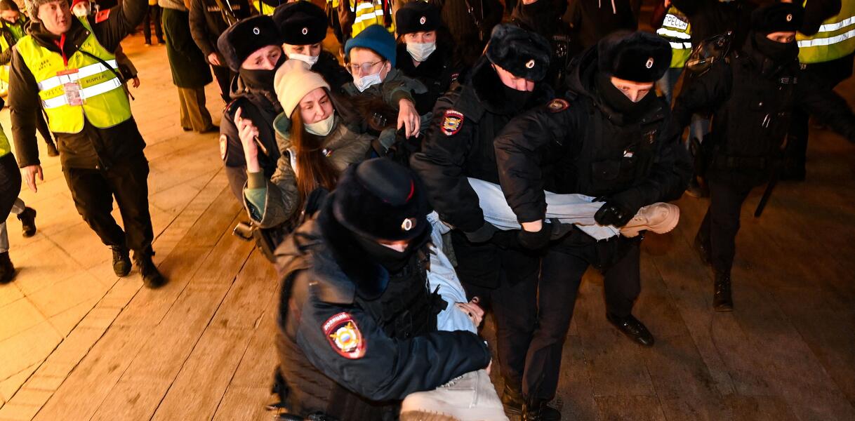 Das Foto zeigt zwei Frauen in einer Menschenmenge, die von sechs Sicherheitskräften an Armen und Beinen weggetragen werden.