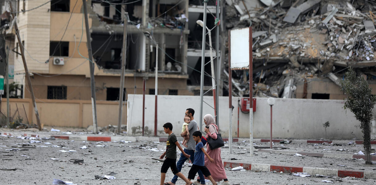Das Bild zeigt eine Familie, im Hintergrund sieht man ein zerstörtes Gebäude