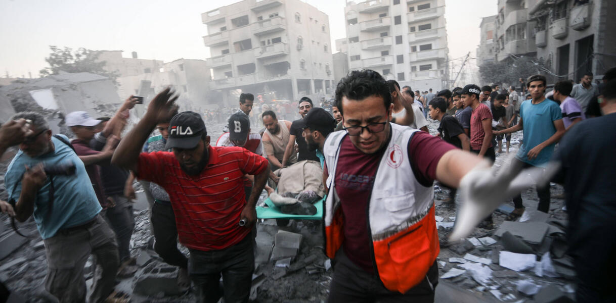 Das Foto zeigt Männer, die einen Mann auf einer Trage tragen, inmitten von Schutt und zerstörten Gebäuden.