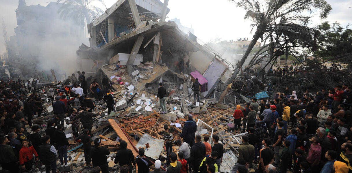 Das Bild zeigt eine Menschenmenge vor einem zerstörten Gebäude