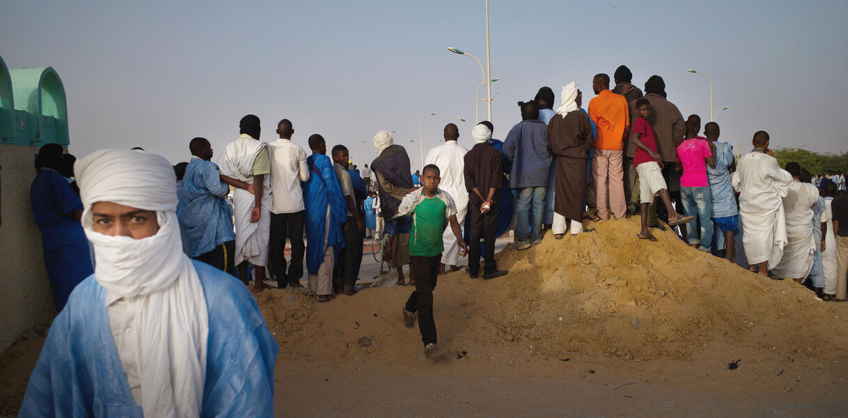 Männer und Jungen in Mauretanien haben sich zum Protest versammelt, sie stehen auf einem kleinen Erdhügel, dahinter Straßenlaternen.