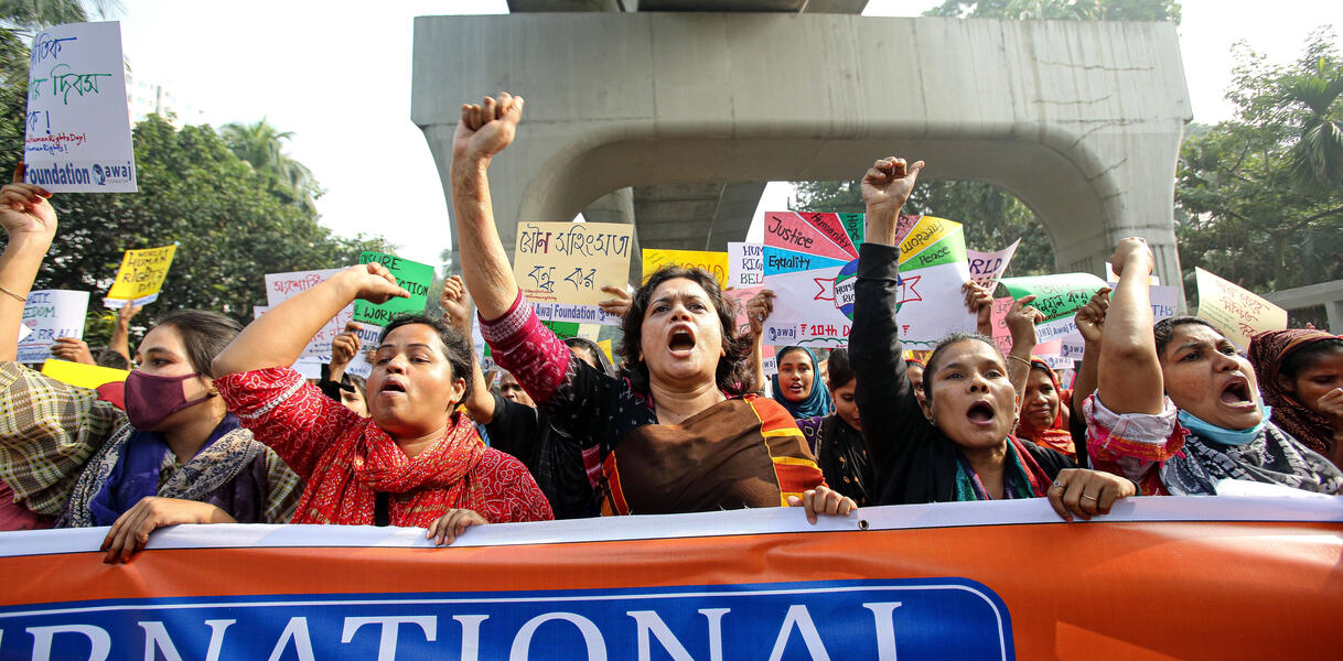 Das Foto zeigt mehrere Frauen bei einer Demonstration, die hinter einem Banner stehen. Einige von ihnen recken die Fäuste nach oben.