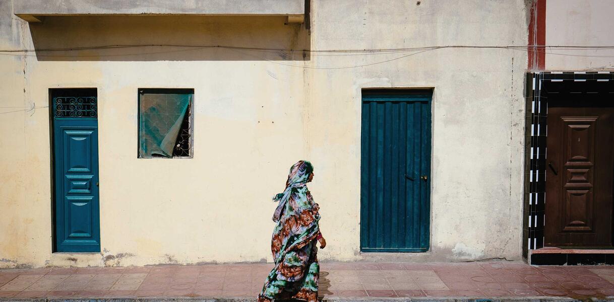 Eine Frau in traditioneller Kleidung geht in der Westsahara eine Straße entlang.