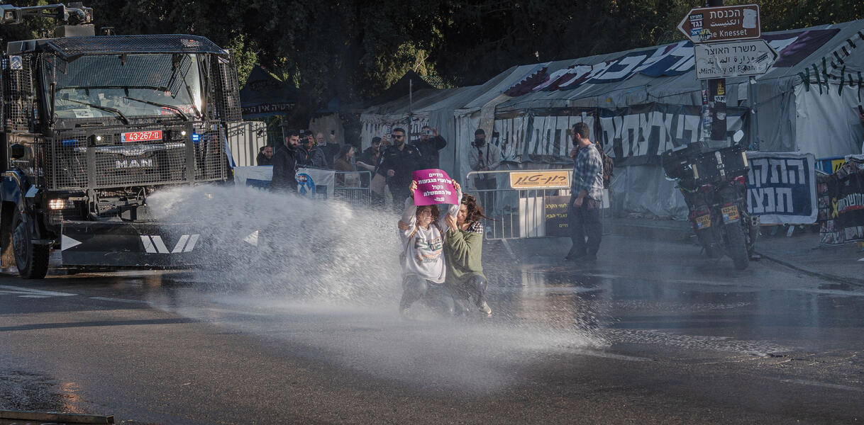 Menschen auf einer Straße stehen im Strahl eines Wasserwerfers, Szene aus einem Protest gegen die Todesstrafe in Jerusalem