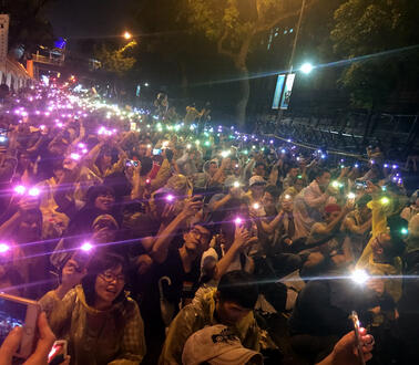 Eine Protestgruppe steht mit bunten Lichtern in der Dunkelheit zusammen