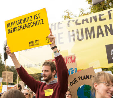 Ein Mann steht in der Menge von Demonstranten und hält ein Schild hoch mit der Aufschrift "Klimaschutz ist Menschenschutz"