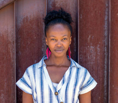 Porträtfoto von Trixie Munyama, die vor einer rostigen Metallwand steht und ernst in die kamera blickt.