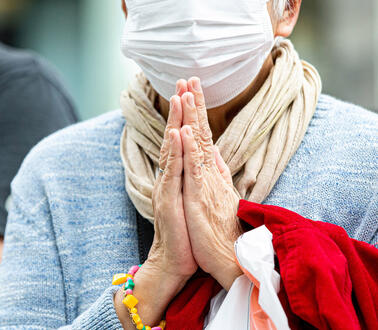 Eine ältere Frau mit Mundschutz faltet ihre Hände zum Gebet
