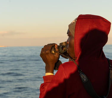Ein Mann mit Fernglas sieht auf das offene Meer.