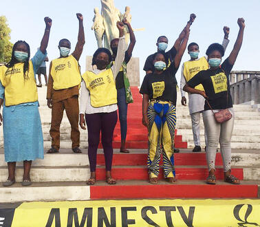 Mehrere Personen auf einer Treppe mit Amnesty-T-Shirts heben die linke Hand, davor ein Amnesty-Banner