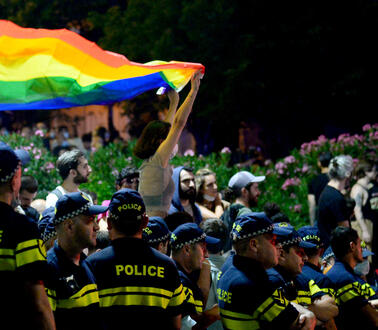 Eine Frau hält eine Regenbogenfahne über den Kopf. Sie ist von uniformierten Polizisten umgeben.