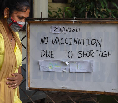 Das Bild zeigt eine Frau rechts im Bild, die an einem Schild vorbeiläuft mit der Nachricht "Vaccine Shortage"
