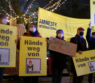 Das Foto zeigt mehrere Masken tragende Personen, die neben einem Amnesty-Banner mehrere Plakate mit der Aufschrift "Hände weg von Memorial" halten.