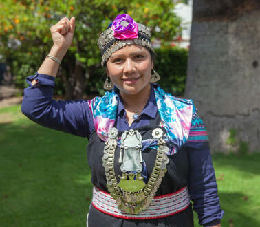 Eine junge Frau in der traditionellen Kleidung der chilenischen Mapuche hält ihre rechte Hand zur Faust geballt nach oben.