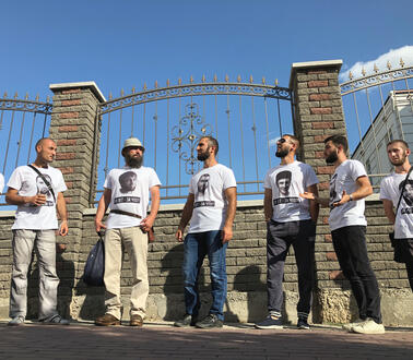 Männer in T-Shirts stehen vor einem Zaun vor einem Gerichtsgebäude.