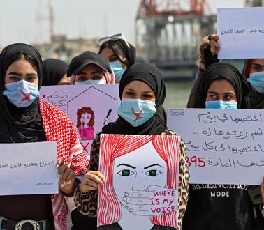 Das Foto zeigt eine Gruppe von sieben Frauen, die Kopftücher und Mundschutz tragen und Schilder mit arabischer Schrift und Zeichnungen vor sich halten.