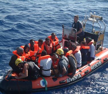 Das Bild zeigt ein Rettungsboot im Meer, mit vielen Menschen, die Rettungswesten tragen 