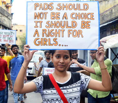 Das Bild zeigt eine junge Frau bei einer Demonstration, die ein Schild nach oben hält