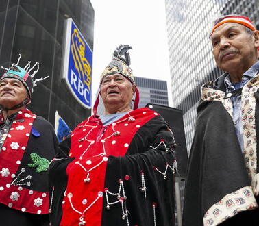 Drei Männer in traditioneller Bekleidung stehen vor einem Gebäude und schauen in die Kamera