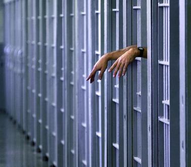 Eine Person hält ihre Hände aus den Gitterstäben ihrer Gefängniszelle.